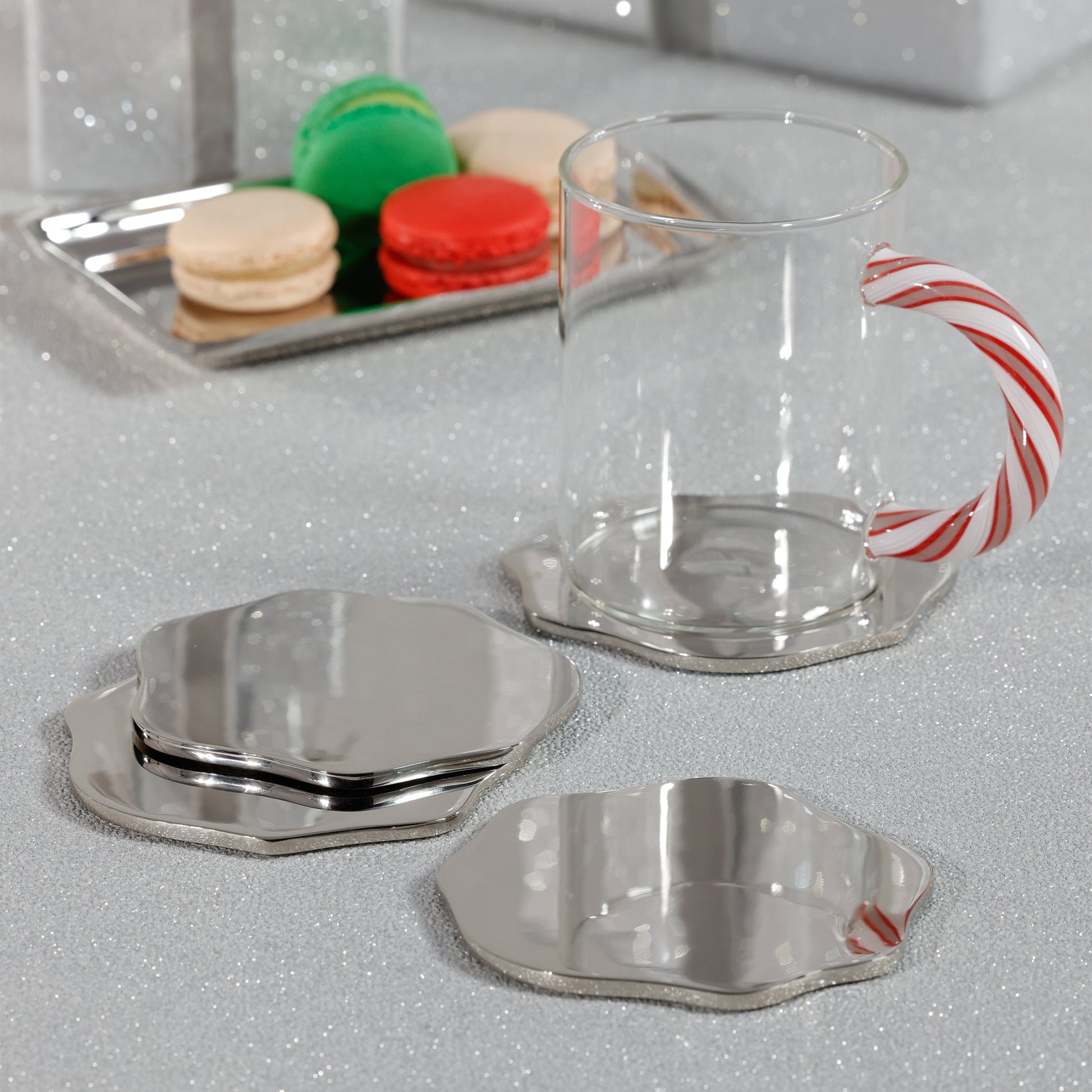 Clear glass mug with candy cane design handle on a reflective surface, with macarons in the background.