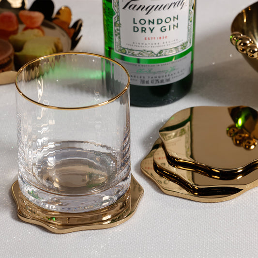 Clear glass with gold rim on a coaster next to a bottle of Tanqueray London Dry Gin.