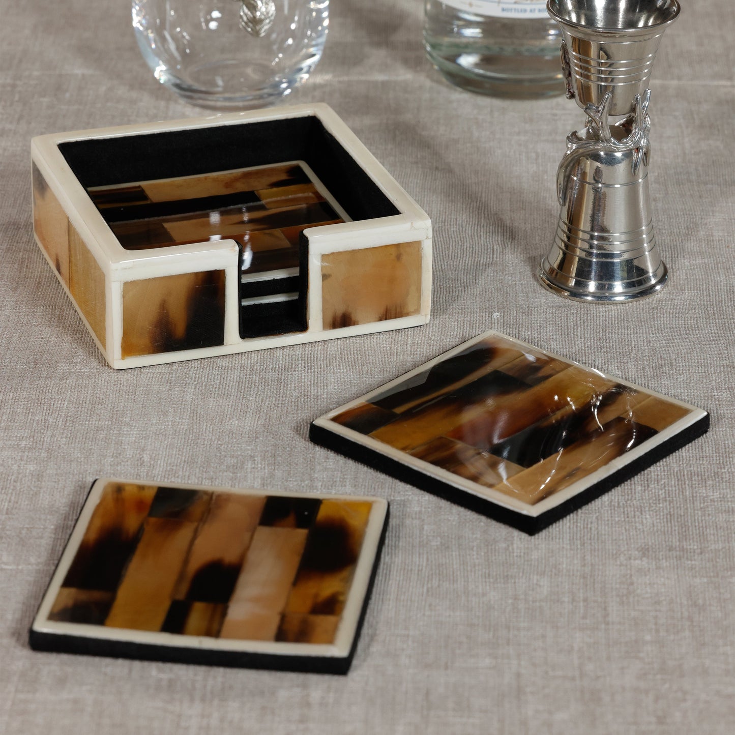 Set of tortoiseshell coasters with a holder on a textured surface.