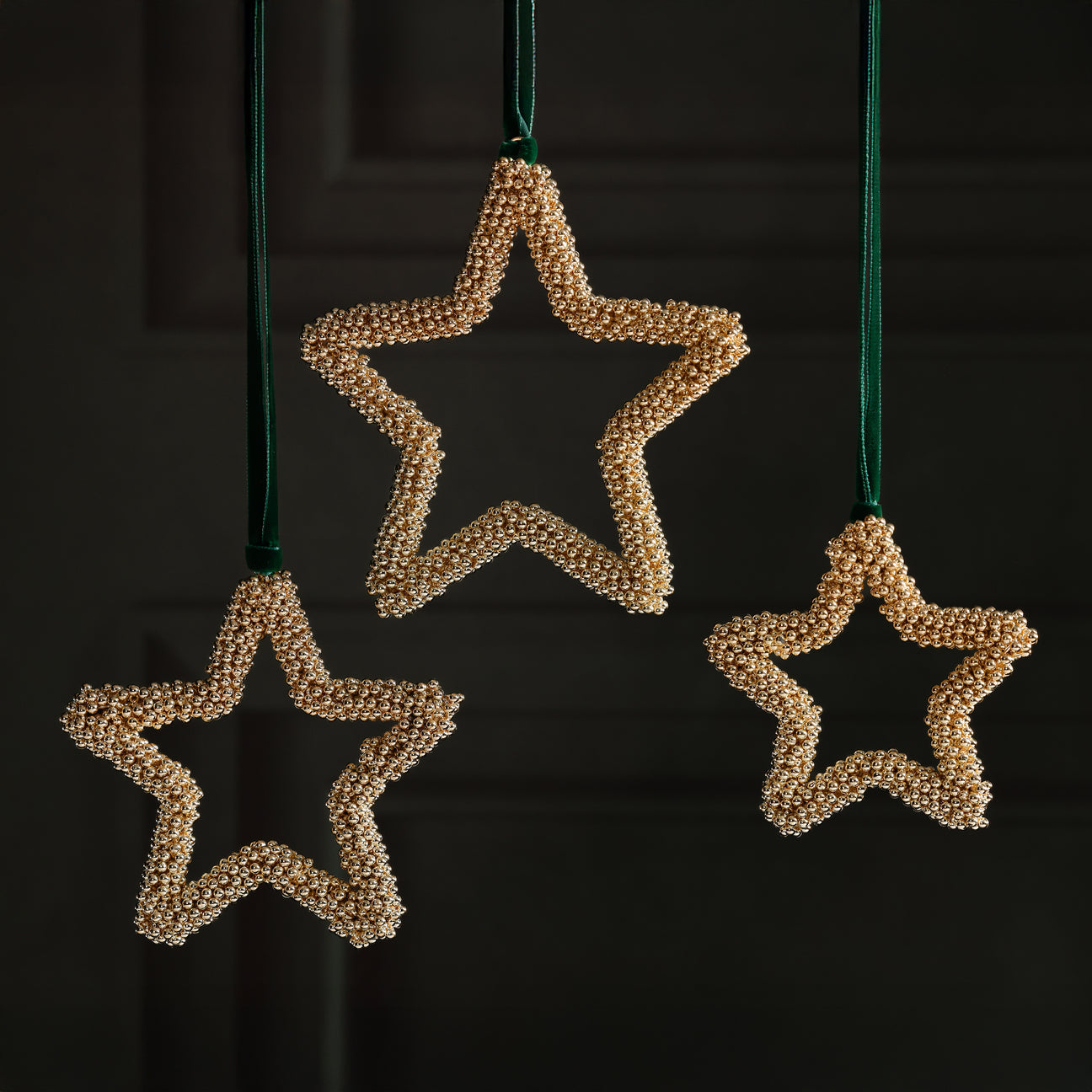 Three star-shaped decorations made of beaded material hanging against a dark background.