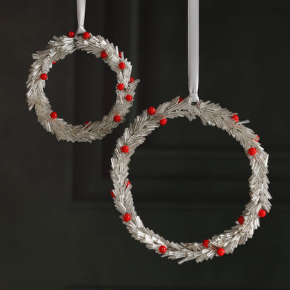 Two silver wreath ornaments with red berries on a black background