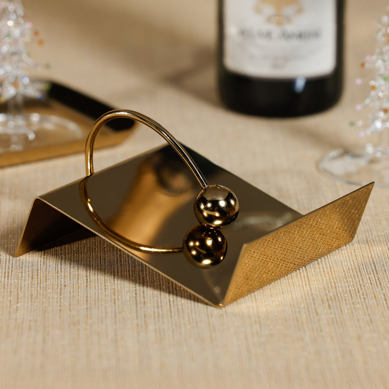 Gold decorative napkin holder on a textured surface with a bottle in the background