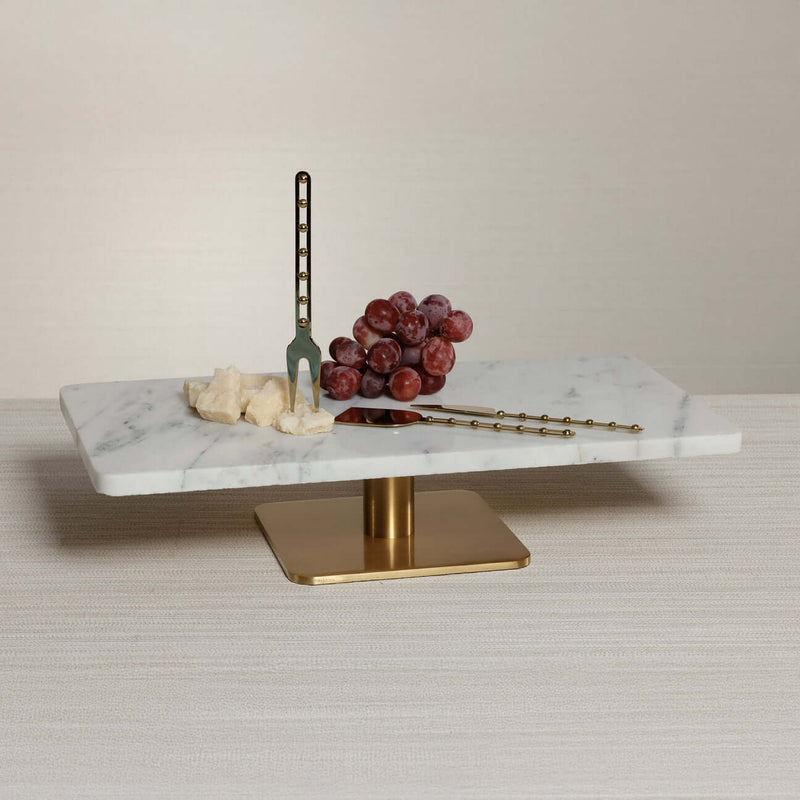 Bodega Cheese and Charcuterie Marble Serving Tray with cheese, grapes, and gold utensils on a table.