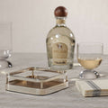 Linea Cocktail Napkin Holder displayed with cocktail glass and tequila bottle on a stylish table.