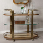 Sloane Oak Wood Oval Bar Cart featuring antique brass frame and glass shelves, perfect for stylish entertaining.
