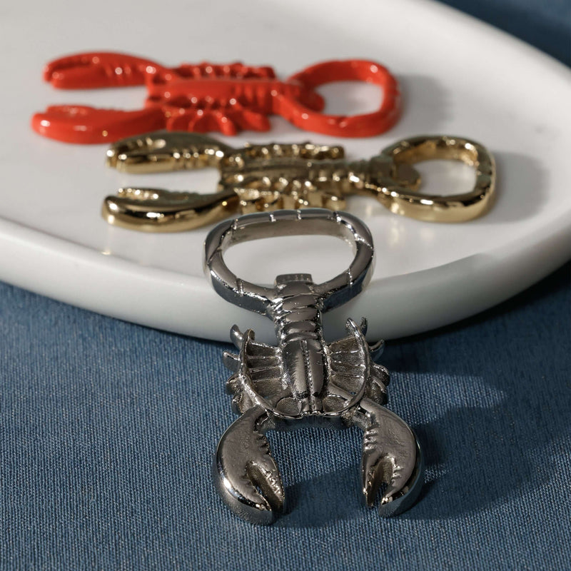 Lobster Bottle Opener in glossy red, polished gold, and silver on a plate, showcasing unique coastal design.