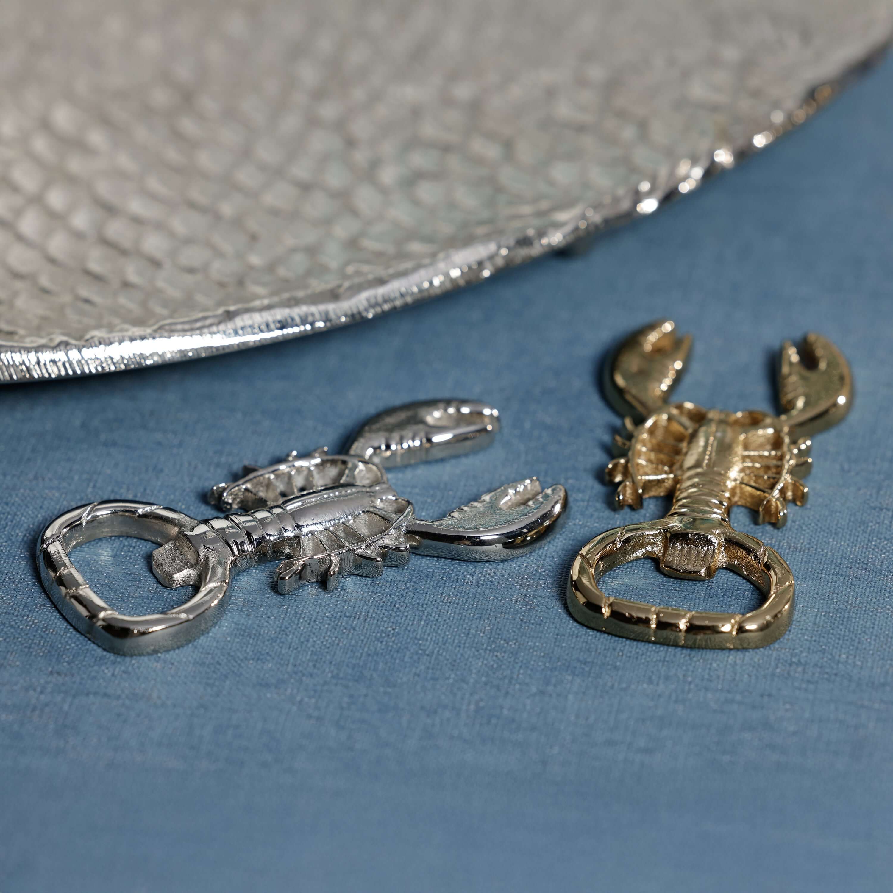 Lobster Bottle Opener in polished silver and gold finishes displayed on a table with a textured plate.