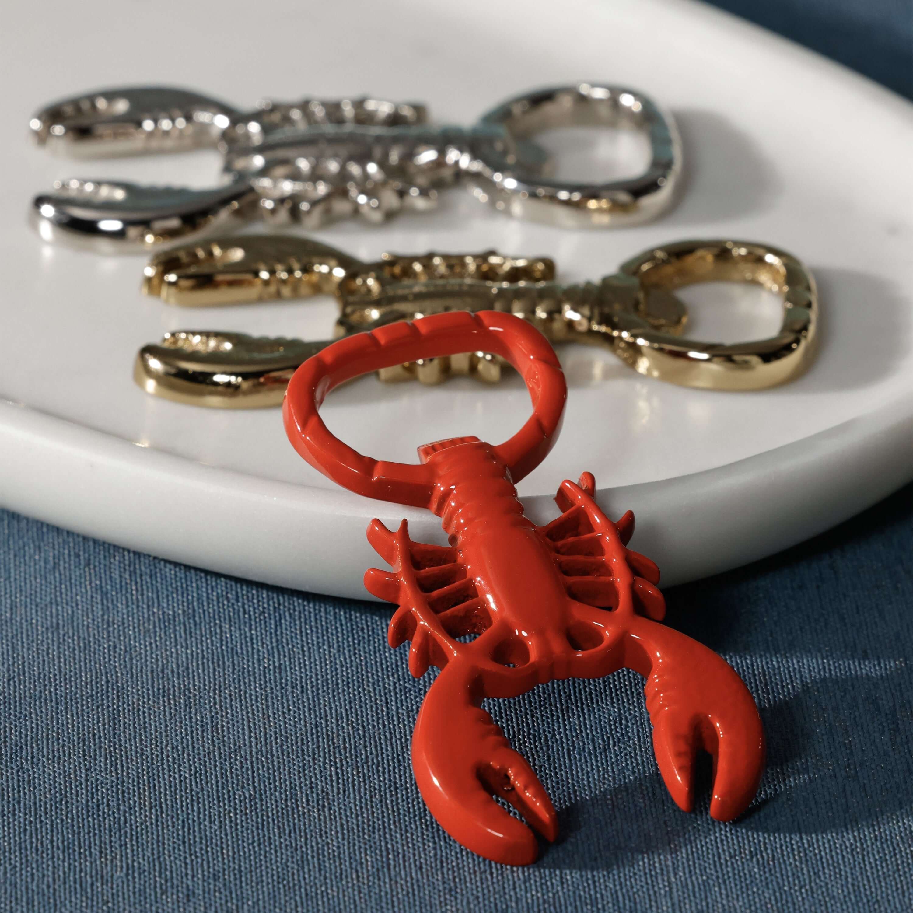 Lobster Bottle Opener in glossy red with silver and gold versions on a plate, showcasing coastal bar accessories.