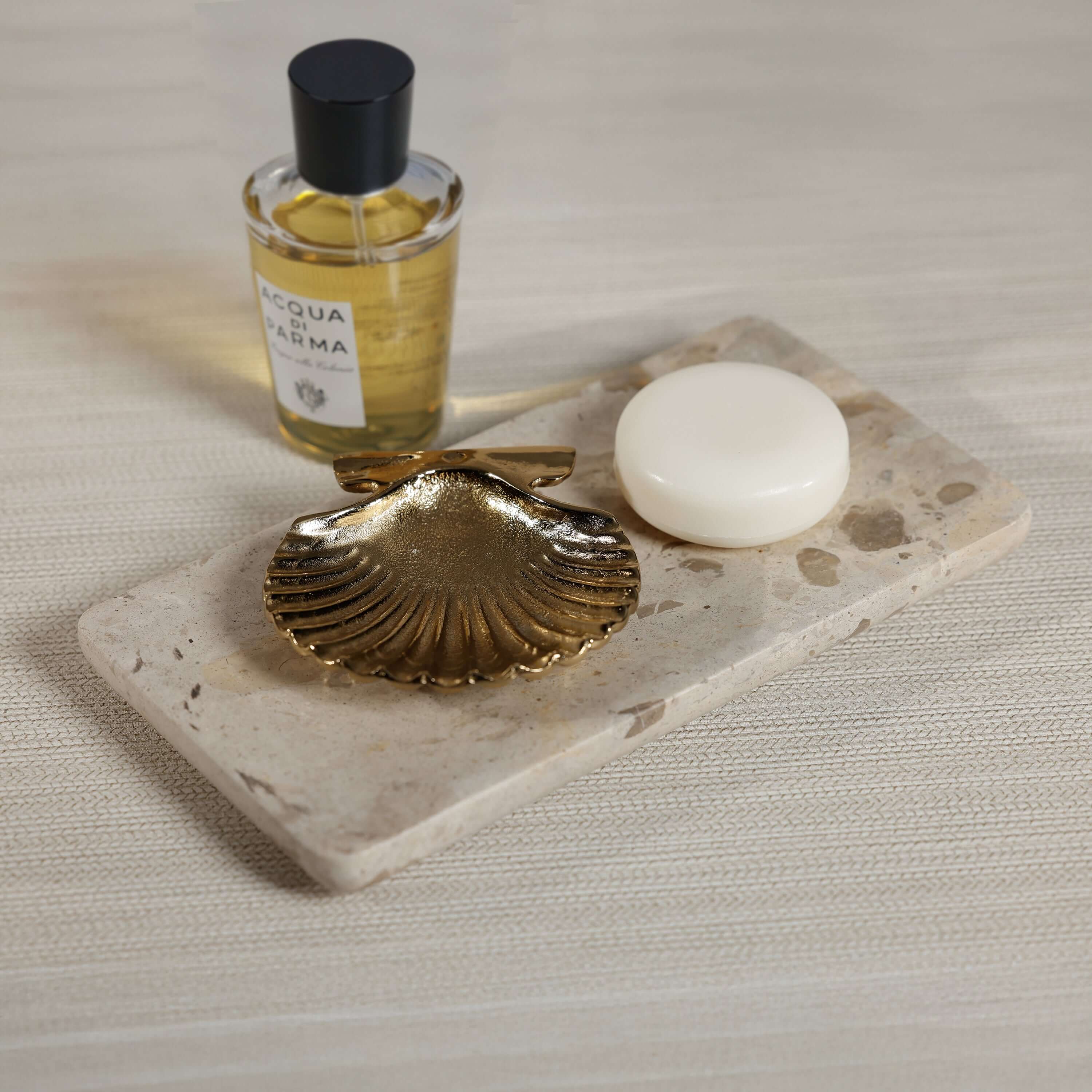 Crema Fossil Marble Bath Collection displayed with gold shell dish, soap, and fragrance bottle on a marble tray.
