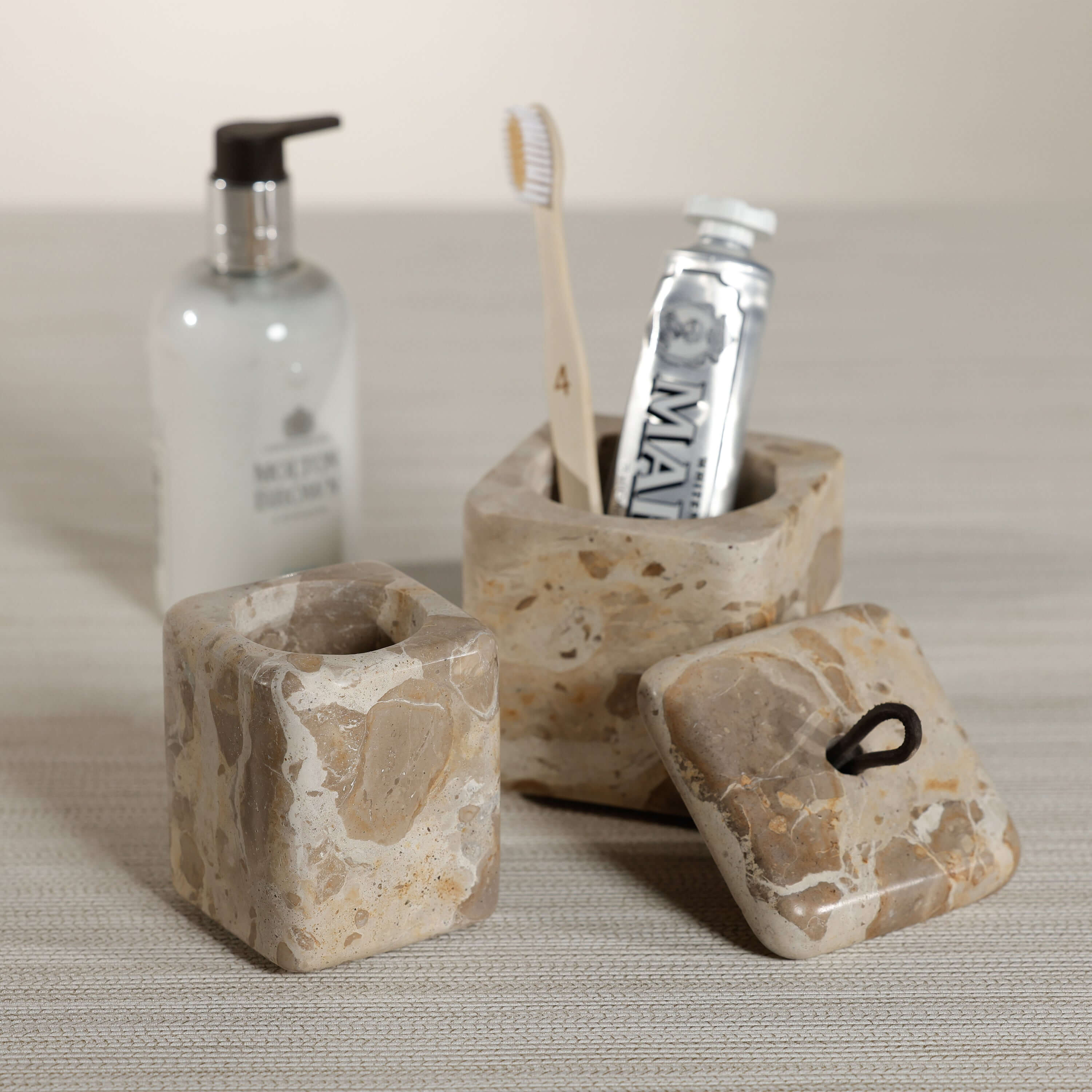 Crema Fossil Marble Bath Collection accessories including toothbrush holder and lidded jar in natural marble.