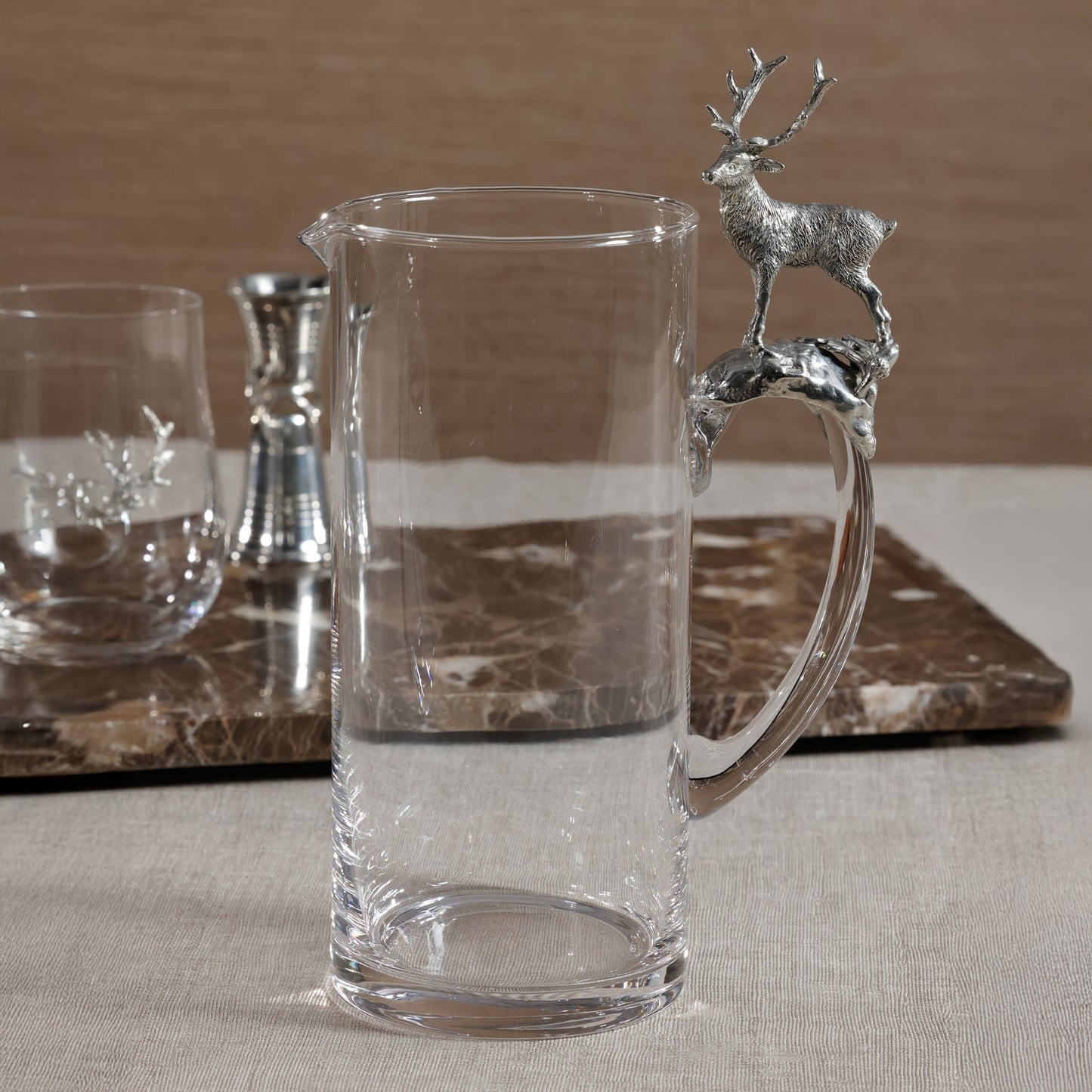 Clear glass pitcher with deer handle on a marble surface