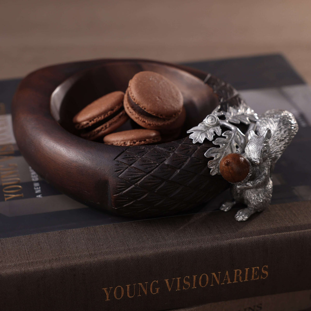 St. Anton Wood Nut Bowl w/Pewter Squirrel with macarons on a brown table.