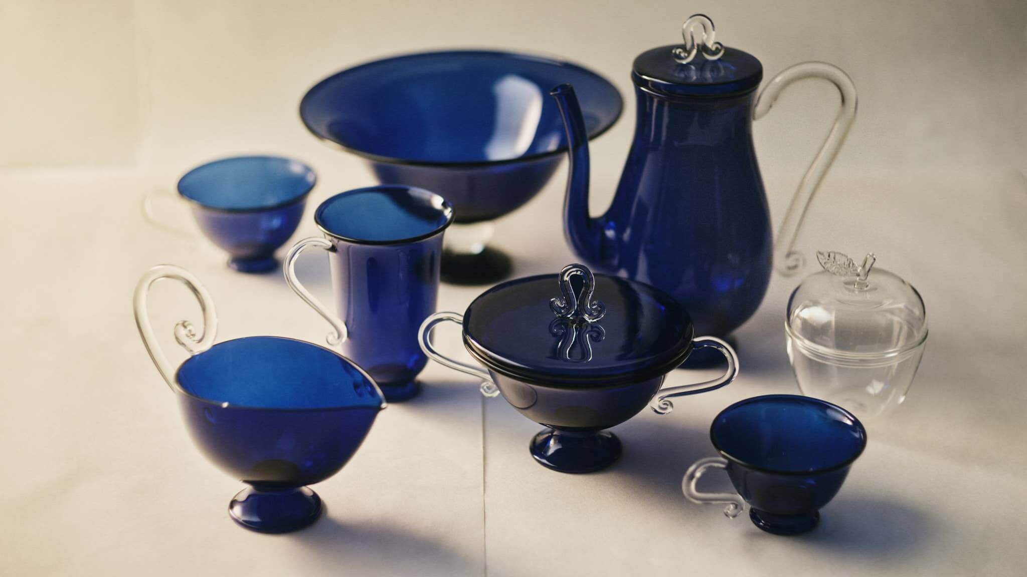 A collection of blue and clear glass dishware, featuring a Fruit Bowl, Blue/Clear, with cups and a teapot.
