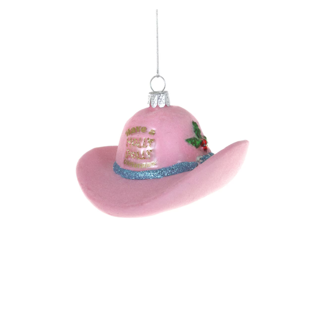 A pink felt cowboy hat Christmas ornament with gold glitter text reading 'have a holly dolly christmas, a blue glitter band, and a small holly accent, hanging against a white background.